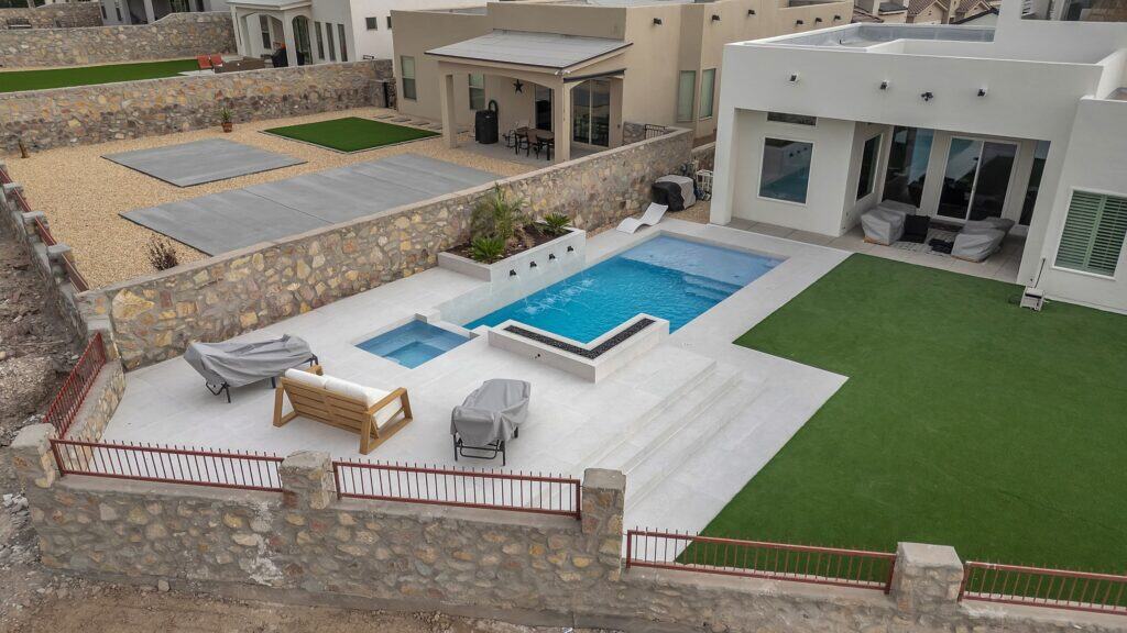 Aerial view of a modern backyard with a custom rectangular pool, raised spa, fire feature, and turf lawn designed by Eraland’s Custom Pools in El Paso, TX.