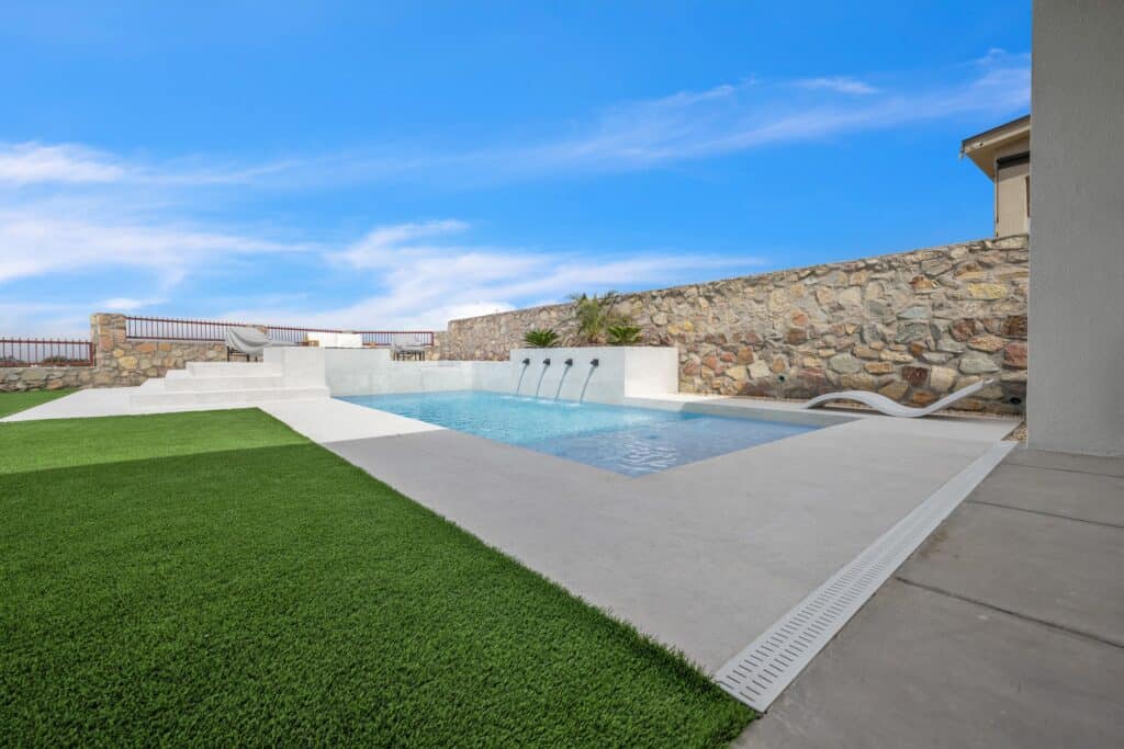Wide view of a modern rectangular pool framed by concrete decking, turf, and a stone privacy wall in El Paso, TX, built by Eraland’s Custom Pools.