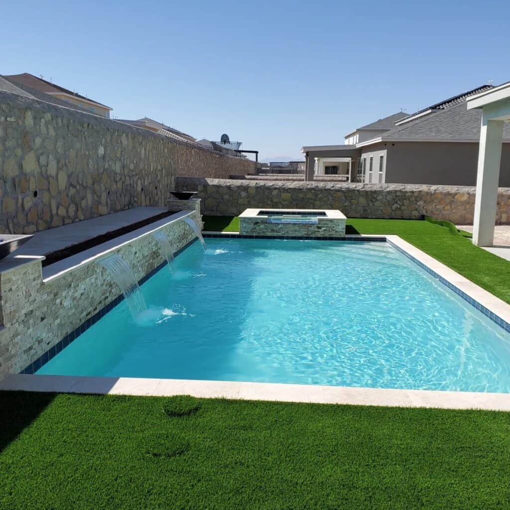 Wide view of the full backyard showing the pool, raised spa, turf areas, and stone walls at an Eraland’s Custom Pools project in El Paso, TX.